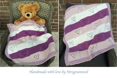 Gestrickte Babydecke in Lila, Rosa und Weiß mit Herzlochung, teilweise über einem Teddybären drapiert.