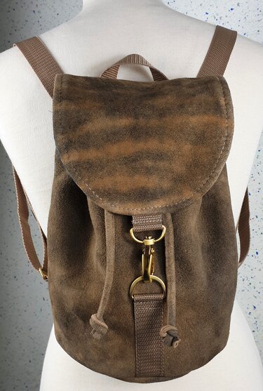 Nahaufnahme eines braunen Rucksacks in genarbter Wildlederoptik mit Kordelzug, Überschlag und messingfarbenen Karabinern auf einer Schneiderpuppe