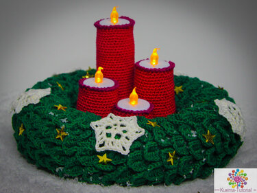 Chunky green crochet wreath with white snowflakes, gold star sequins and four red crochet covers over flameless LED tealights