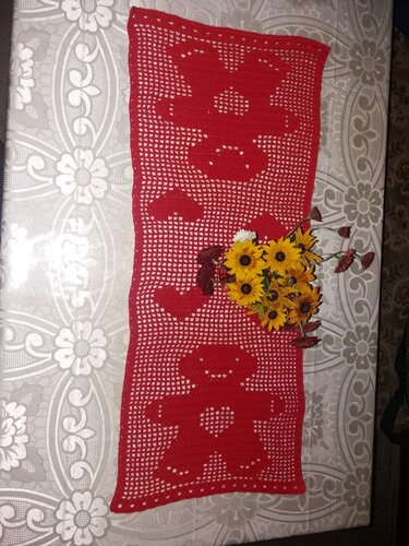 Roter gehäkelter Tischläufer im Filet-Muster mit Bär- und Herzmotiven auf hell gemusterter Tischdecke und Blumenstrauß