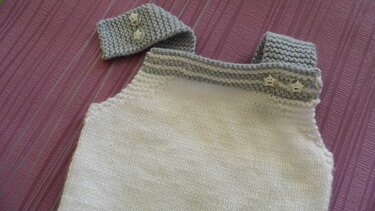 weiß gestrickter Trägerstrampler mit grauen knöpfbaren Trägern und passendem Stirnband