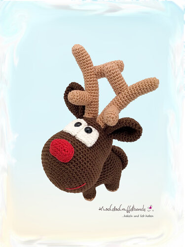 Gehäkeltes braunes Rentier-Amigurumi mit roter Nase, weißen Augen und hellbraunem Geweih vor hellblauem Hintergrund.