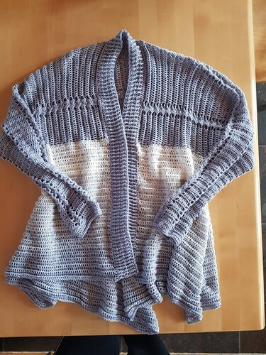 Offener gehäkelter Damen-Cardigan in Grau und Weiß auf Holztisch