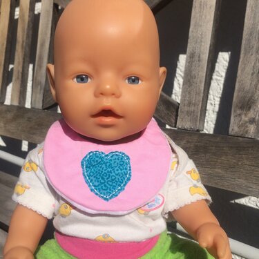 Puppe trägt rosa Lätzchen mit blauem Herz