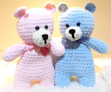 Zwei gehäkelte Amigurumi-Teddys, einer rosa mit Herzanhänger, einer blau mit karierter Schleife