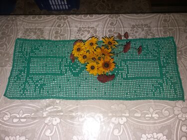Grüner gehäkelter Tischläufer im Filetmuster mit gelben Blumen darauf