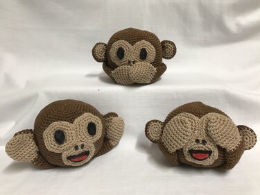 Drei braun-beige gehäkelte Amigurumi-Affen auf hellem Hintergrund; vorne links lächelnd, vorne rechts mit den Augen bedeckend, hinten neutral