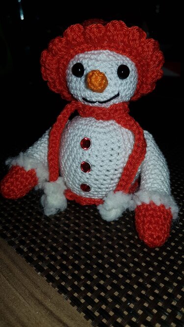 Gehäkelte Schneemann-Figur in Weiß mit roter Mütze, rotem Schal und oranger Nase