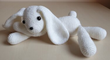 Weißer gehäkelter Amigurumi-Hase liegend mit langen Schlappohren