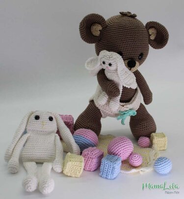 Gehäkelter brauner Teddybär mit kleinem weißen Häschen, sitzender weißer Hase, pastellfarbene Häkelbälle und Häkelwürfel