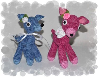 Zwei gehäkelte Amigurumi-Rehe, blaues Reh mit weißer Schleife und rosa Reh mit Rosenapplikation