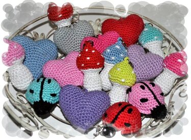 Nahaufnahme vieler bunter, gehäkelter Schlüsselanhänger in Form von Herzen, Pilzen und Marienkäfern in einer Schale.
