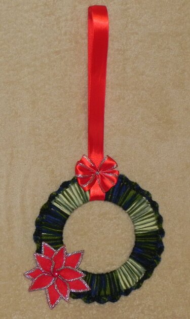 Handgehäkelter Weihnachtskranz in Grün und Blau mit rotem Weihnachtsstern und roter Satinschleife.