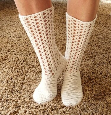 Weiße gehäkelte wadenhohe Socken mit feinem Lochmuster auf hellem Teppich.