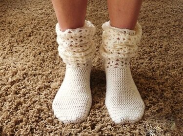 Cremefarbene gehäkelte Damensocken mit lockerem Rüschbündchen an Damenbeinen auf Teppichboden