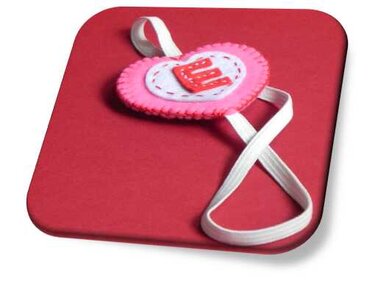 Pinkes Filzherz mit rotem E und weißem Elastikband auf rotem Untergrund