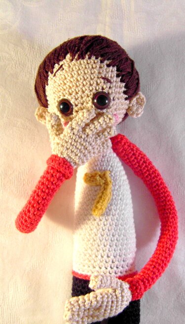 Gehäkelte Amigurumi‑Puppe mit Hand vor dem Mund, großen Augen und roten Armen