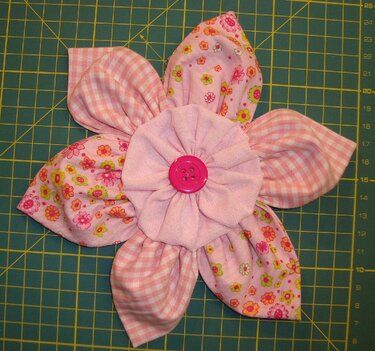 Rosa Stoffblüte-Applikation mit fünf Blütenblättern und pinkem Knopf auf Schneidematte