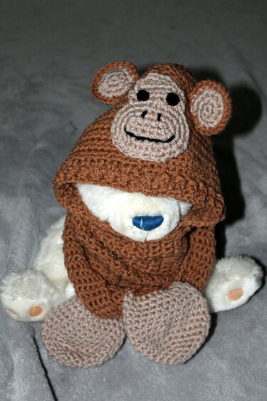 Plüschtier trägt braun-beige gehäkelte Kapuzenmütze mit Affengesicht und Ohren