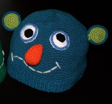 Blaue gehäkelte Kindermütze mit applizierten Augen, oranger Nase und grünen Ohren