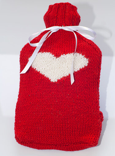Roter gestrickter Wärmflaschenbezug mit weißem Herz und weißer Schleife