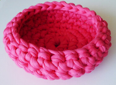 Runder gehäkelter Korb in leuchtendem Fuchsia aus dickem Textilgarn auf hellem Untergrund.