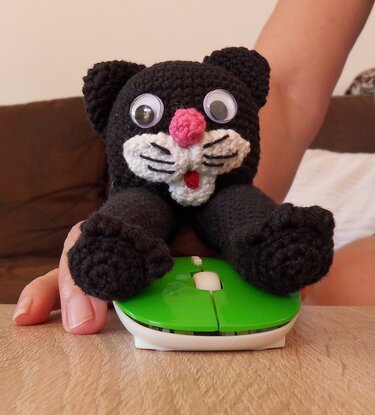 Schwarze gehäkelte Katzen-Fingerpuppe mit weißer Schnauze, rosa Nase und Wackelaugen auf grüner Computermaus