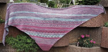 Dreieckstuch gestrickt in Rosa und Hellblau mit Streifen, Ajour- und Strukturmustern an einer Steinmauer drapiert