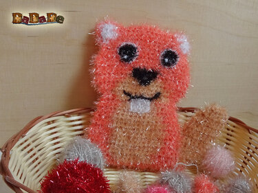 Gehäkelte Tierfigur in Orange und Beige mit flauschiger, schimmernder Struktur, sitzend in einem Weidenkorb mit Dekokugeln.