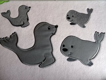 Vier applizierte graue Robben in unterschiedlichen Posen auf hellem Stoff