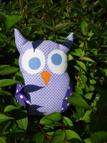 Gepunktete Stoff-Eule mit applizierten weißen Augen und orangefarbenem Schnabel zwischen grünen Blättern