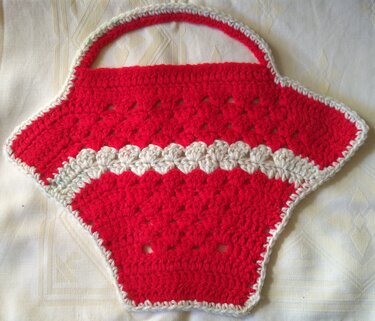 Roter gehäkelter Topflappen in Korbform mit cremefarbener Muschelkante und Henkel auf hellem Stoff.