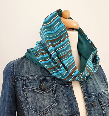 Gestreifter Loopschal in Blau- und Brauntönen auf einer Schneiderpuppe mit Jeansjacke.