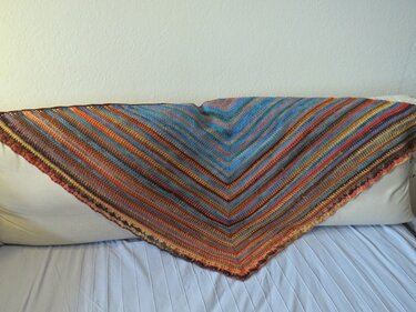 Gehäkeltes Dreieckstuch mit bunten diagonalen Streifen, auf einem Kissen drapiert