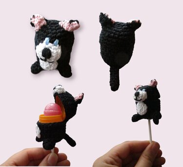 Vier Ansichten eines kleinen schwarzen gehäkelten Katzen-Anhängers mit weißem Gesicht und rosa Ohren; eine Ansicht geöffnet zeigt einen runden Behälter, eine Hand hält einen Anhänger an einem Stab.