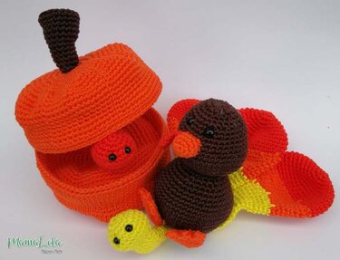 Gehäkelter brauner Truthahn mit buntem Fächerschwanz und orangefarbene Kürbisbox mit Deckel vor weißem Hintergrund