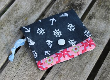 Genähtes kleines Portemonnaie aus zwei Stofflagen mit maritimem Außenstoff, geblümtem Innenstoff, Druckknopf und Band auf Holzbank