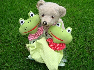 Teddybär mit zwei grünen Frosch-Schmusetüchern mit Rüschenkragen auf grünem Rasen