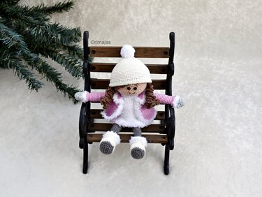 Gehäkelte Amigurumi-Puppe mit Bommelmütze auf Holzbank
