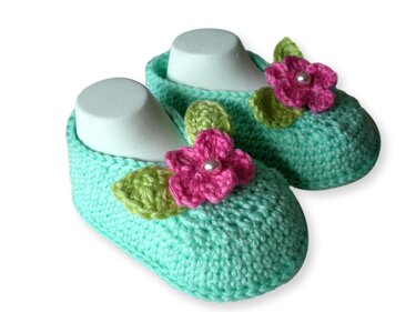 Ein Paar mintgrüner, gehäkelter Babyschuhe mit rosa Blüten und grünen Blättern auf weißen Schuhformen.