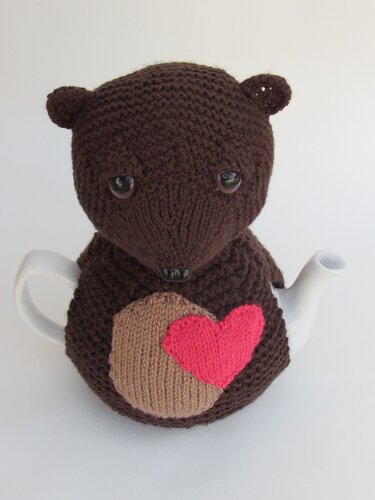 Dark brown knitted bear tea cozy with pink heart appliqué on a teapot