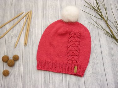 Korallrote gestrickte Mütze mit weißem Bommel und seitlichem Ajourzopf