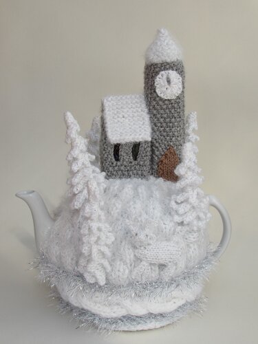 Christmas knitted tea cosy with grey tower, snowy roof, knitted trees and silver fringe on teapot