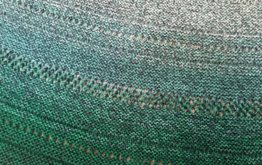 Detailansicht eines halbrunden Stricktuchs mit kraus-rechten Maschen und regelmäßigen Lochreihen in Grünverlauf
