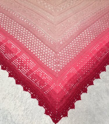 Nahaufnahme eines gehäkelten Dreieckstuchs mit Rosé‑zu‑Rot‑Farbverlauf, Lochmuster und gewelltem Saum.