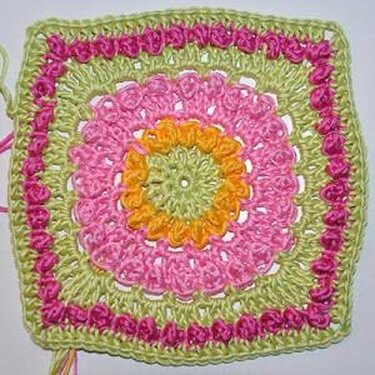 Gehäkeltes Granny Square in Grün, Pink und Orange mit floral wirkendem Kreis in der Mitte und quadratischer Umrandung.