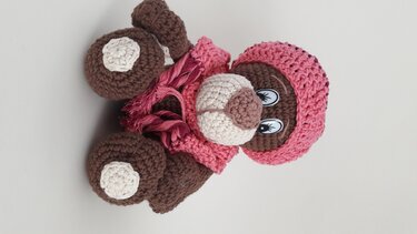 Nahaufnahme eines gehäkelten Amigurumi-Teddybären mit Schnauze, Pfoten und rosa Mütze