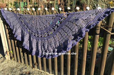Lila gehäkeltes Dreieckstuch mit feinem Spitzenmuster an einem Holzzaun