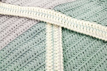 Nahaufnahme einer gehäkelten Babydecke in Pastellgrün und Hellgrau mit segmentierter Struktur und cremefarbener Bordüre