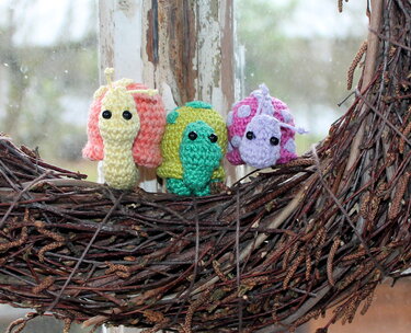 Nahaufnahme von drei gehäkelten Mini-Amigurumi (Schnecke, Käfer, Marienkäfer) auf einem Zweigkranz